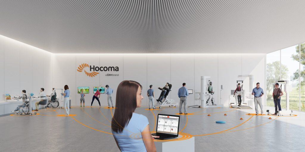 En una espaciosa y moderna clínica, varias personas utilizan máquinas de rehabilitación. Una mujer en primer plano consulta datos en un ordenador portátil. Las paredes muestran el logotipo de "Hocoma".