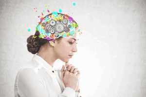 A woman in a white blouse stands in profile with hands clasped, while her head displays a colorful, artistic illustration of a brain with gears and paint splashes.