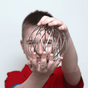 A child in a red shirt holds a spherical metal wire object toward the camera, partially obscuring their face.